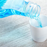 Blue mouthwash being poured into a cup to rinse teeth