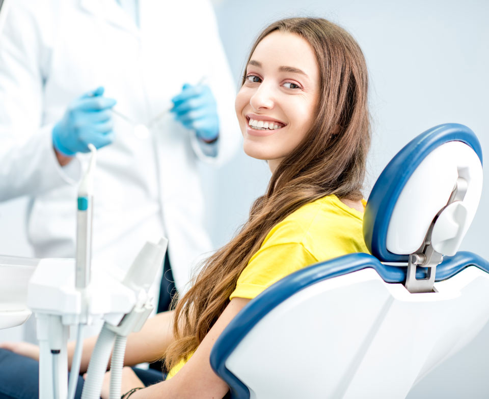 Young brunette woman in a yellow shirt smiles at her dentist in Bellevue, WA