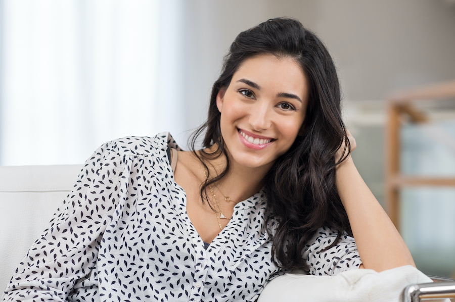 Dark-haired woman smiles while leaning on her hand relaxing at home