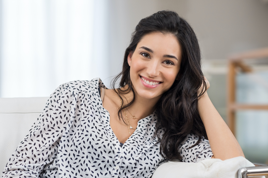 Dark-haired woman smiles while leaning on her hand relaxing at home in Bellevue