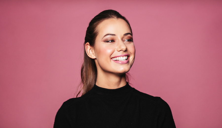 Closeup of a smiling brunette woman in a black shirt against a pink wall in bellevue