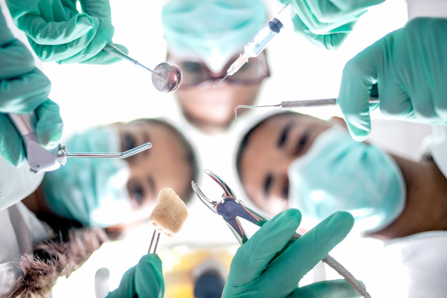 Looking up into the masked faces of 3 dentists performing oral surgery with special dental tools in Bellevue