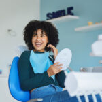 Black woman in a dental chair smiles while holding a hand mirror in Bellevue
