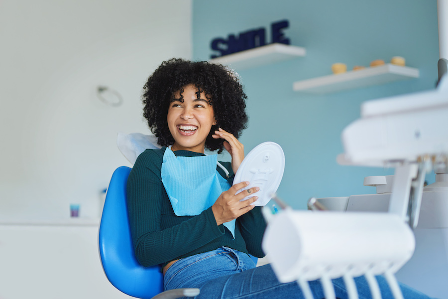 Black woman in a dental chair smiles while holding a hand mirror