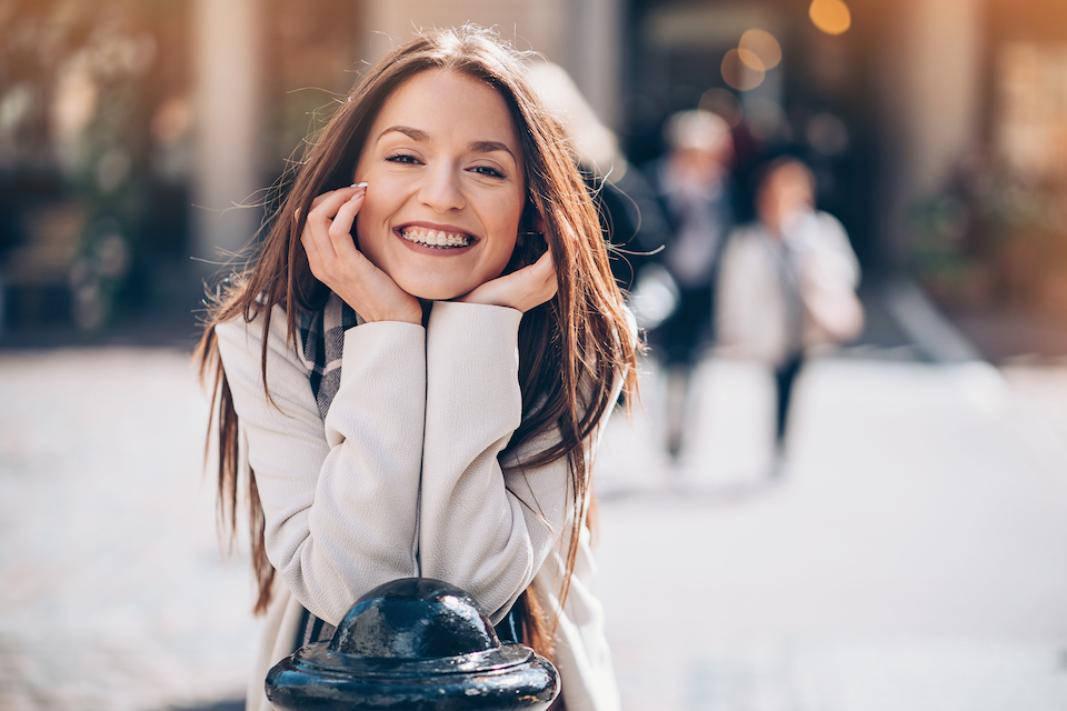 Smiling young woman outdoors in the city undergoing orthodontic treatment.